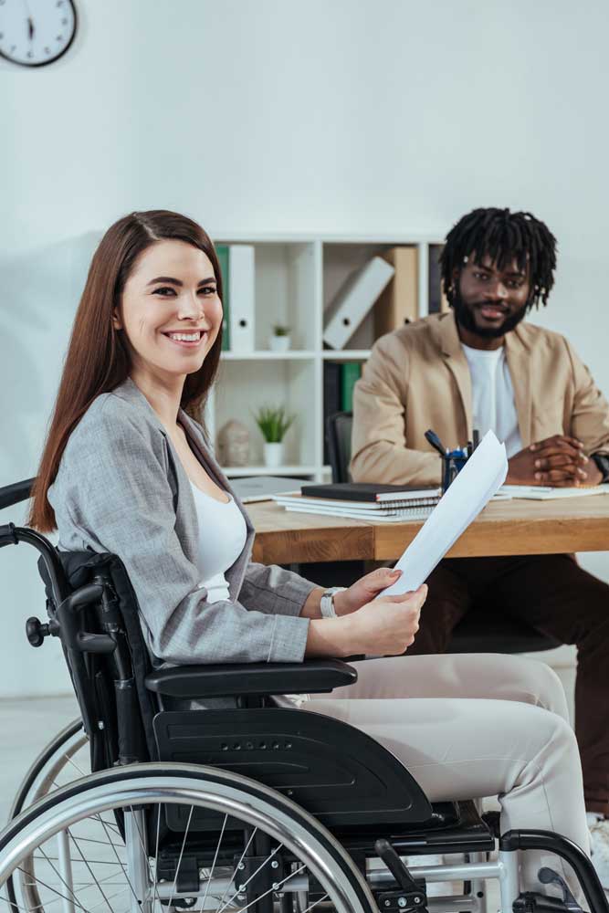An employee in a wheelchair looks over a resume sent by Scion Staffing Minneapolis while her coworker smiles in the background