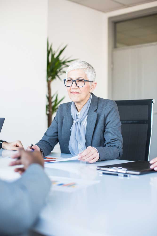 An older female executive with glasses interviews a potential candidate for a position at her Minneapolis paper company